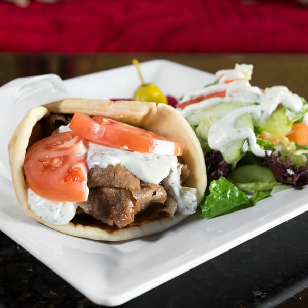 A Mediterranean gyro with meat, tomatoes, and tzatziki sauce, served with a side salad.